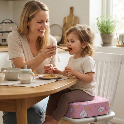 Rehausseur chaise rose sous enfant assis a la table avec maman qui la nourrit